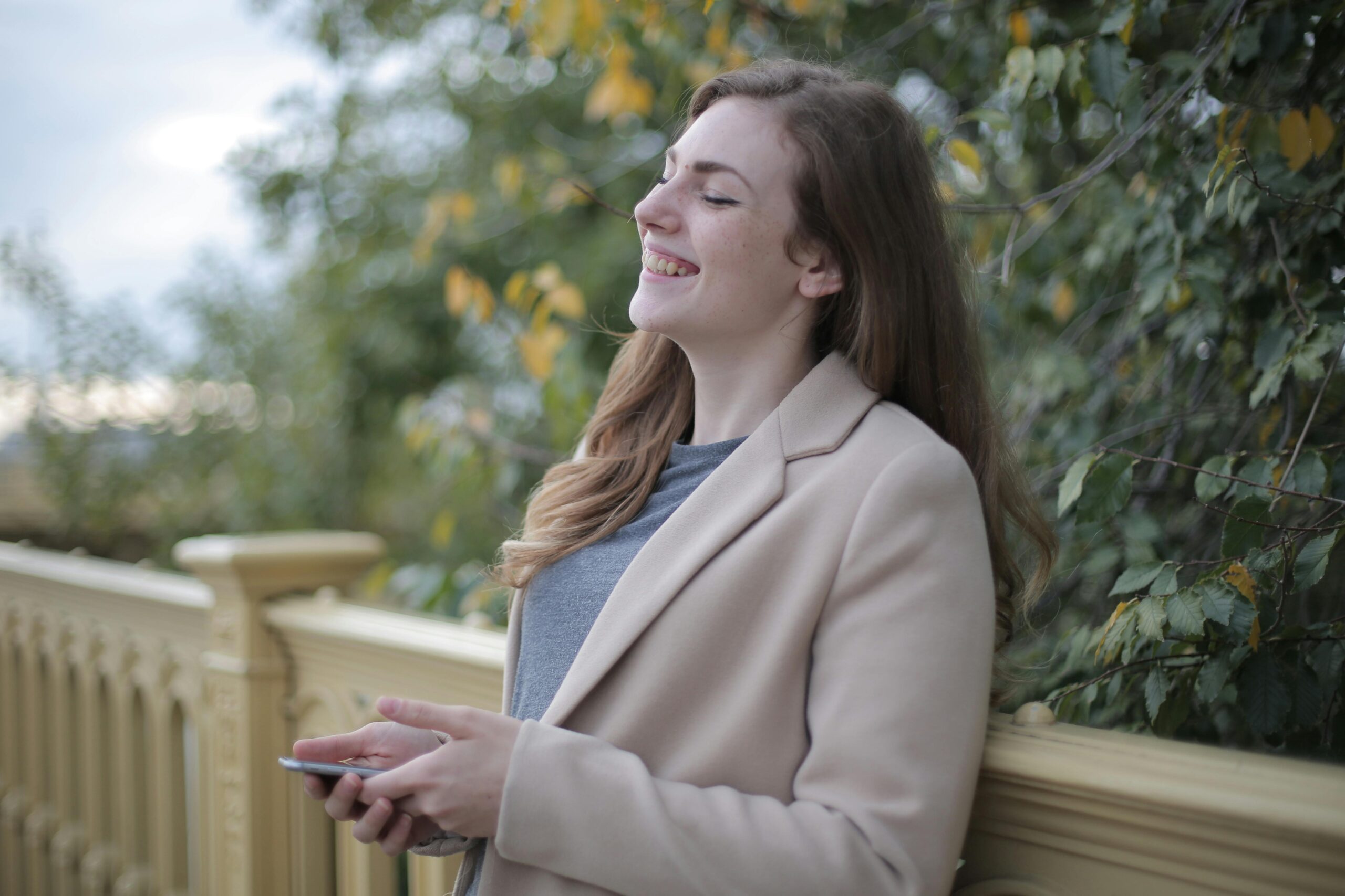 happy lady eyes closed outside on a bench phone in hand